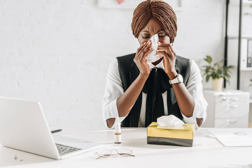 ill afro-americana adulta donna d'affari che soffre di freddo e utilizzando tessuti alla scrivania in ufficio
 - Foto, immagini