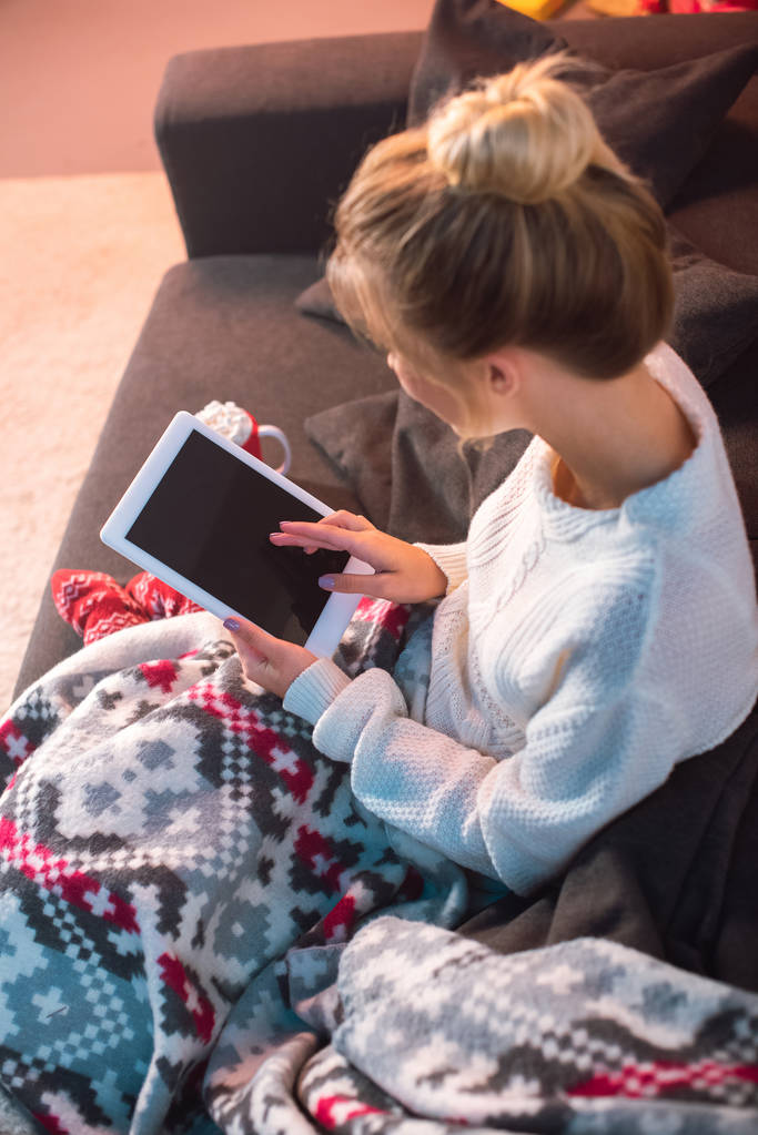 Winkelaufnahme einer jungen blonden Frau, die auf der Couch sitzt und zu Hause ein Tablet benutzt - Foto, Bild
