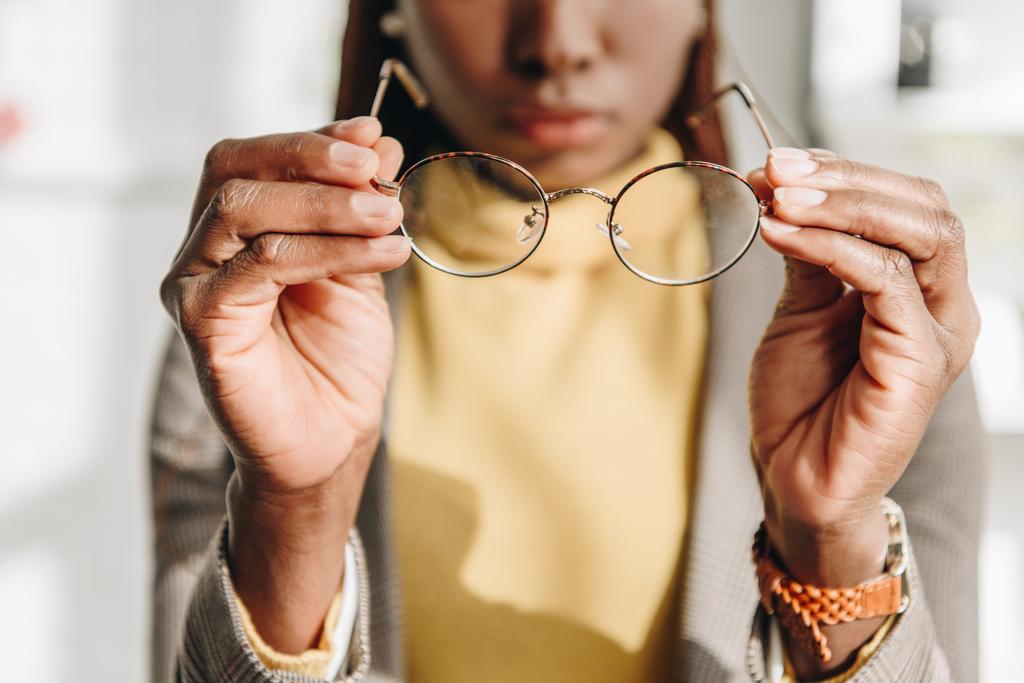 vista recortada de la mujer de negocios adulta afroamericana en ropa formal poniéndose gafas
 - Foto, imagen
