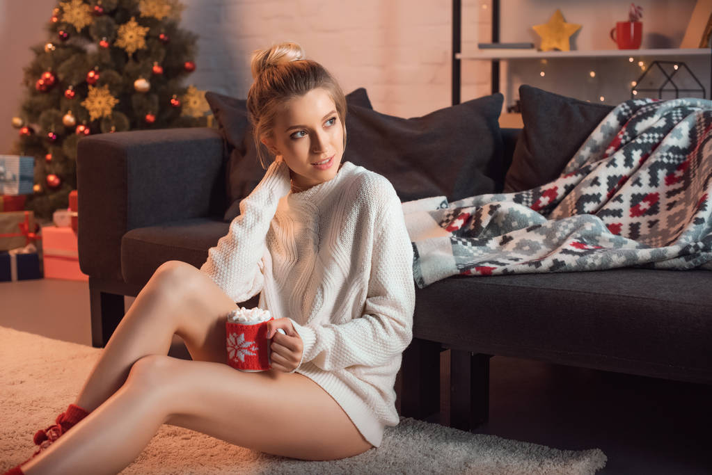 beautiful woman sitting in christmas patterned socks on carpet with mug of cocoa - Photo, Image