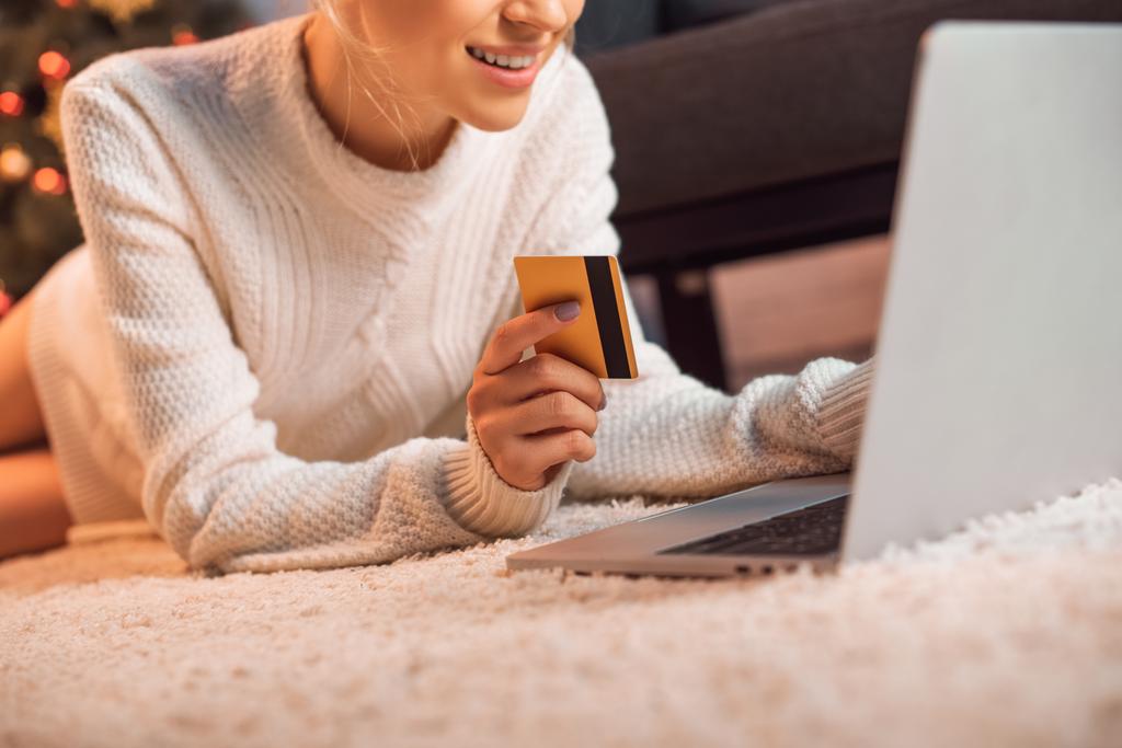 cropped view of woman lying on floor, holding credit card, using laptop and doing online shopping at christmas time  - Photo, Image
