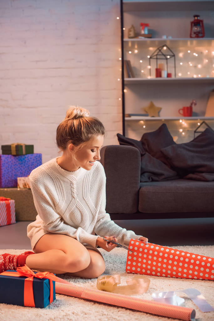 sonriente joven rubia sentada y envolviendo regalos en Navidad
 - Foto, Imagen