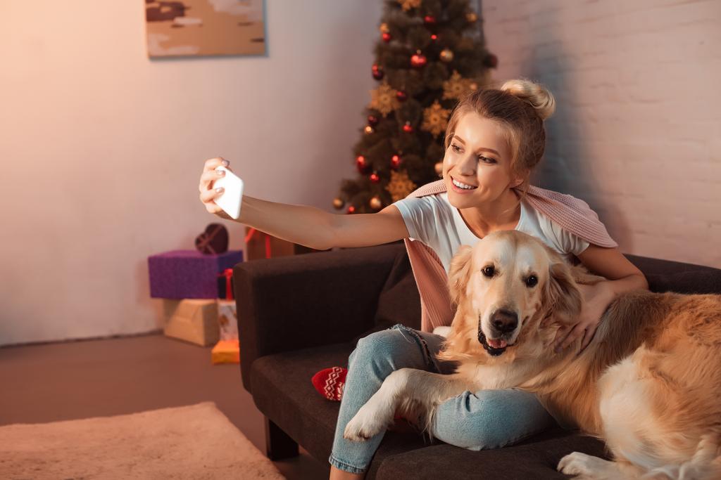 bella giovane donna bionda seduta sul divano con cane golden retriever e scattare selfie su smartphone nel periodo natalizio
 - Foto, immagini