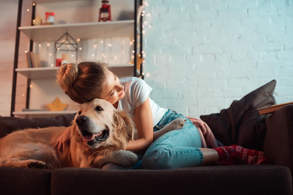 クリスマスの時期にゴールデン ・ リトリーバー犬を抱いてソファに若いブロンドの女性 - 写真・画像
