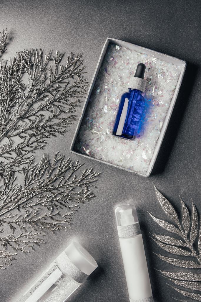 verhoogde weergave van de doos van de gift van Kerstmis met serum, lotion, micellaire water, ingericht takken op zilver - Foto, afbeelding