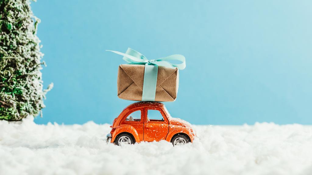 вид сбоку игрушечного красного автомобиля с подарочной коробкой, катающейся по снегу из хлопка на синем фоне
 - Фото, изображение