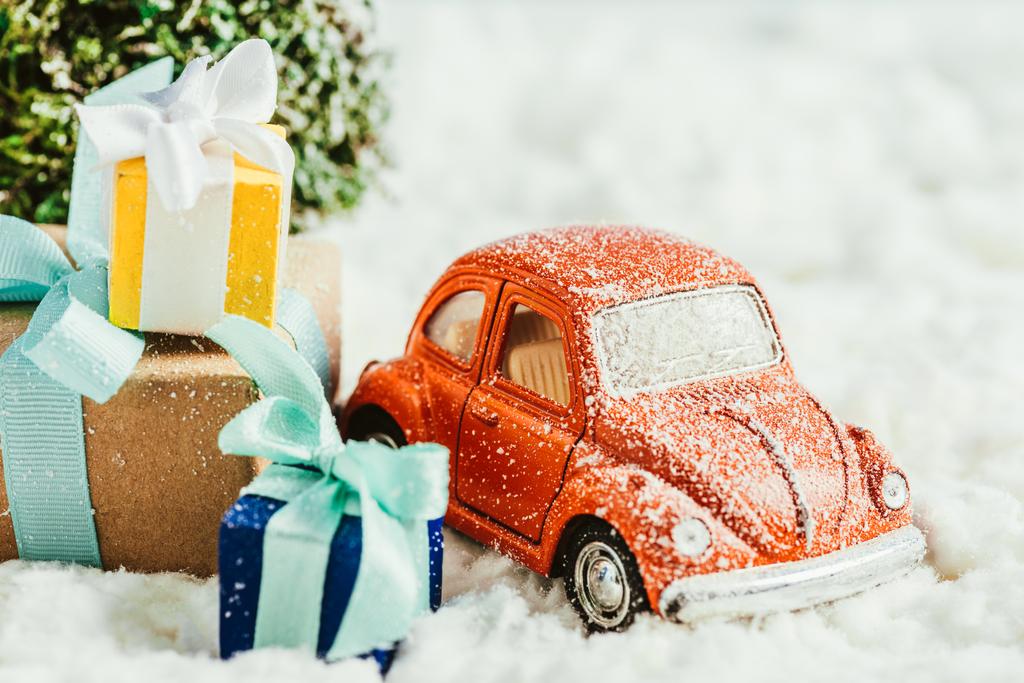 Nahaufnahme eines Spielzeugautos mit Geschenken und Weihnachtsbaum auf Schnee aus Baumwolle - Foto, Bild