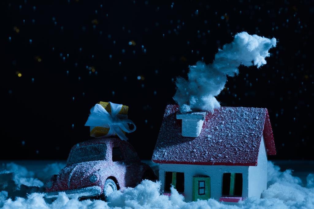 крупным планом игрушечный автомобиль с рождественскими подарками и дом, покрытый снегом ночью
 - Фото, изображение