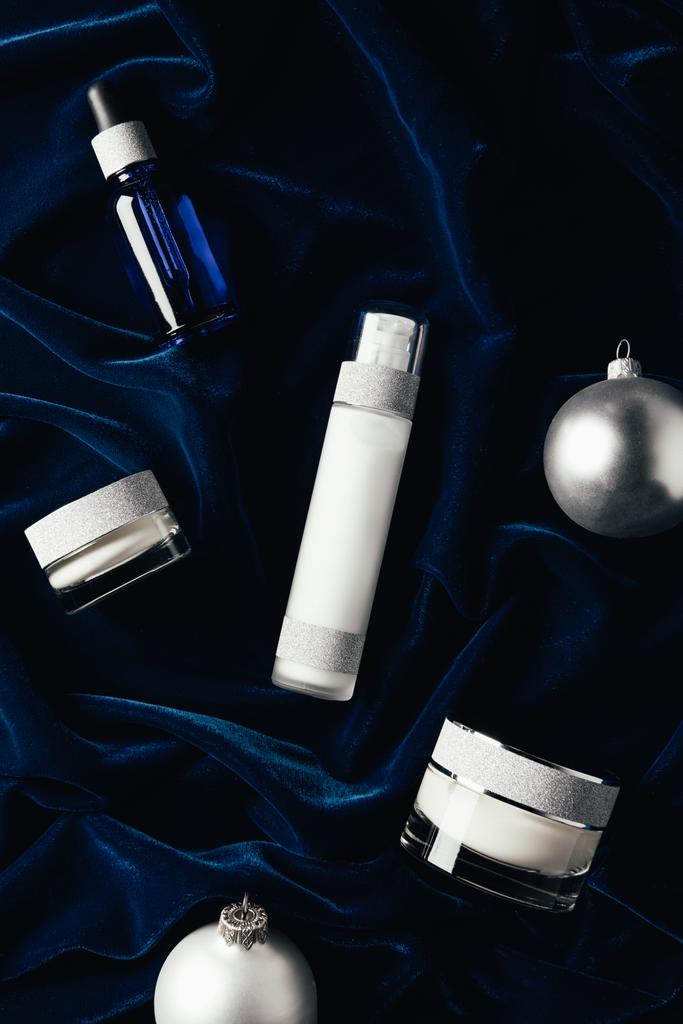 flache Lage mit Schönheitscreme, Serum, Lotion und silbernen Weihnachtskugeln auf Samtoberfläche  - Foto, Bild