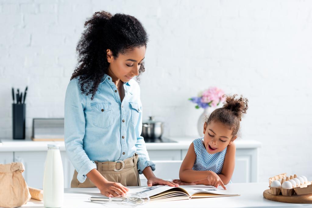 Африканская американская мать и дочь смотрят кулинарную книгу на кухне
 - Фото, изображение
