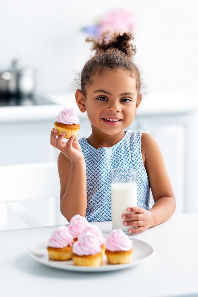 キッチンでケーキとミルクのガラスを保持している、カメラ目線かわいいアフリカ系アメリカ人の子供 - 写真・画像