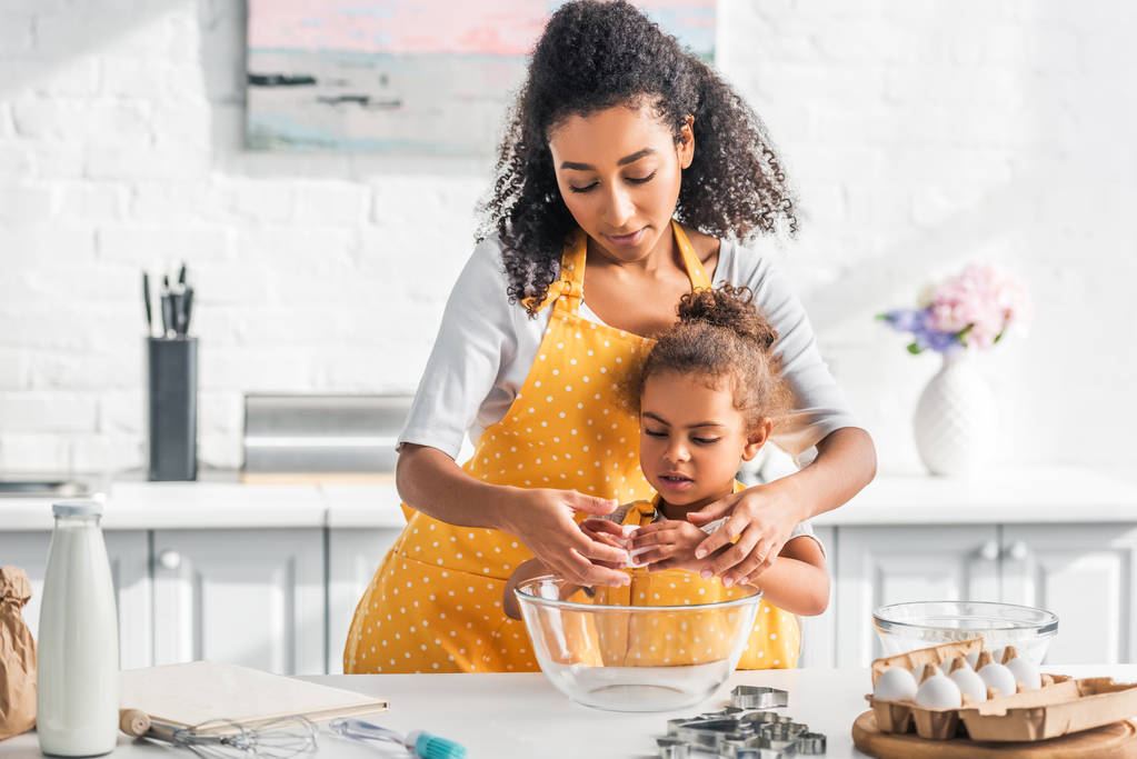 africká americká matka pomáhá dcera lámání vejce na přípravu těsta v kuchyni - Fotografie, Obrázek