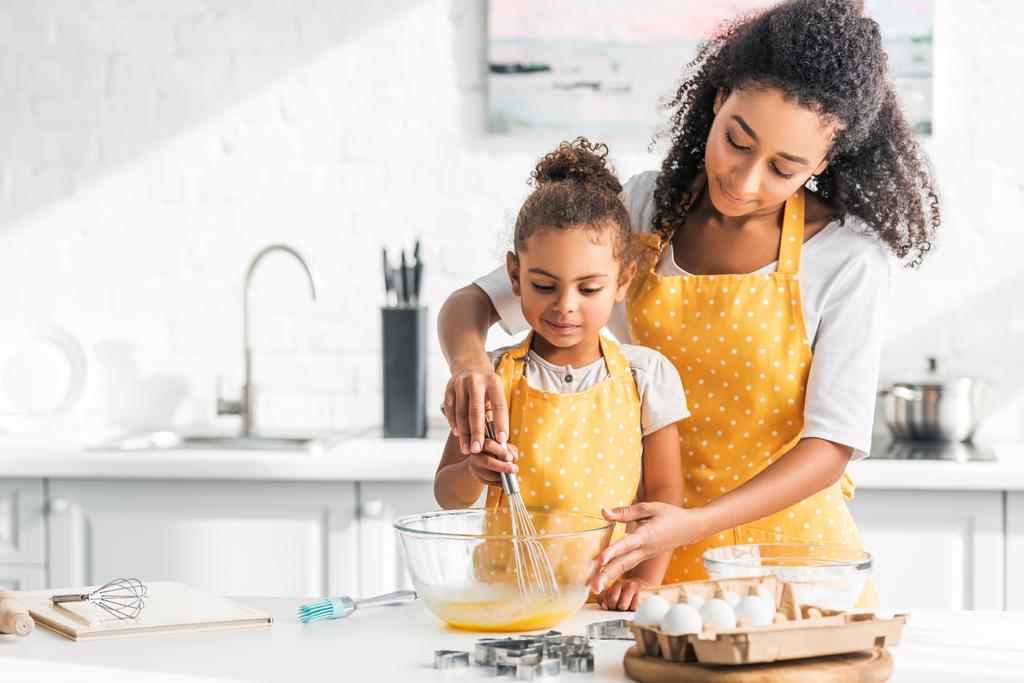 Afrikanisch-amerikanische Mutter hilft Tochter beim Eier schlagen für hausgemachtes Dessert in der Küche - Foto, Bild