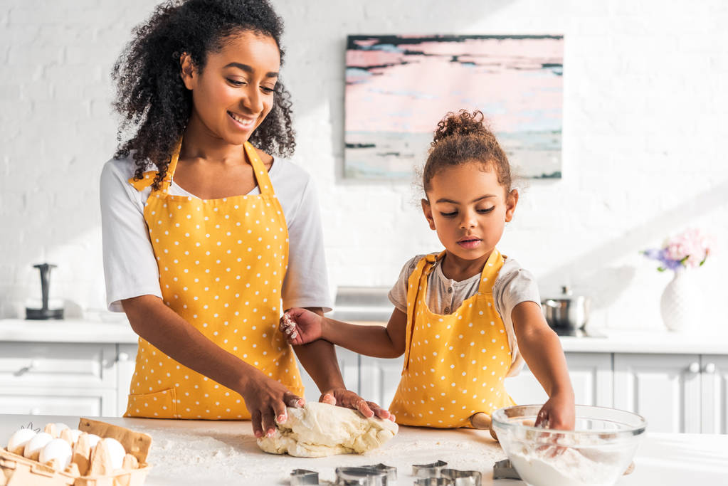 Улыбающиеся африканская американская мать и дочь месят тесто для десерта на кухне
 - Фото, изображение