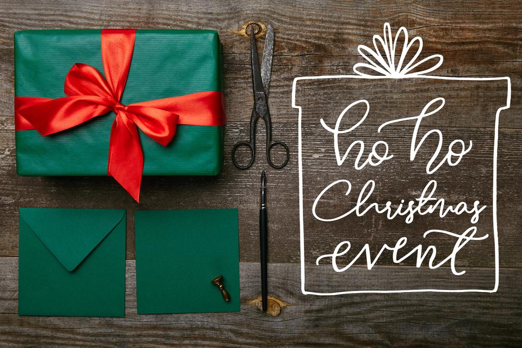 плоский узор с завернутым рождественским подарком с красной лентой, ножницами и конвертами для поздравительной открытки на деревянной поверхности с надписью "хо хо хо рождественское событие"
 - Фото, изображение