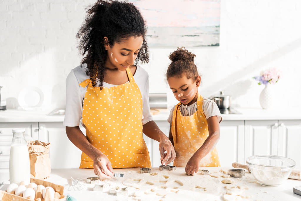 african american matka i córka w żółte fartuchy przygotowanie ciasteczka z formy w kuchni - Zdjęcie, obraz