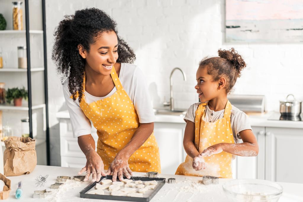 usmívající se africká americká matka a dcera připravuje soubory cookie a při pohledu na sebe v kuchyni - Fotografie, Obrázek