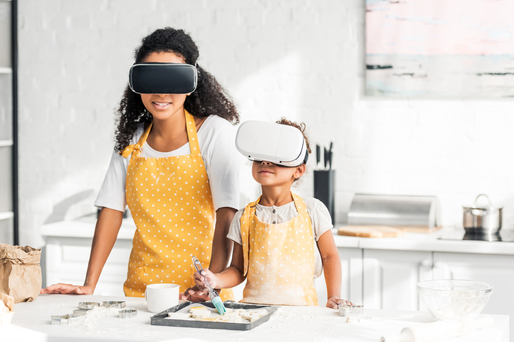 africká americká matka a dcera použití olej na nepečený sušenky s headsety pro virtuální realitu v kuchyni - Fotografie, Obrázek