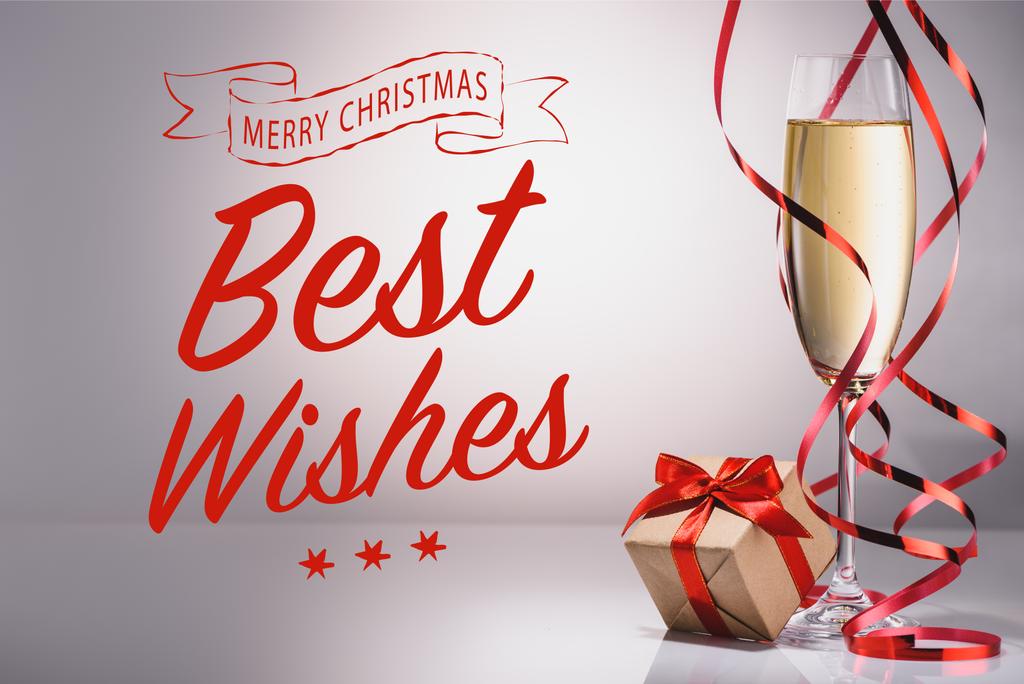 ποτήρι σαμπάνιας και τυλιγμένο δώρο σε γκρι φόντο με «Ευχές» και χαρούμενα Χριστούγεννα γράμματα - Φωτογραφία, εικόνα