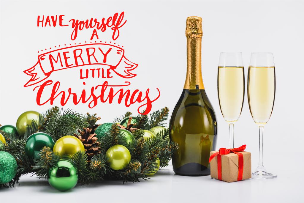 μπουκάλι και ποτήρια της σαμπάνιας, Χριστουγεννιάτικο στεφάνι και δώρο σε λευκό φόντο με έμπνευση «οι ίδιοι ένα merry little Χριστούγεννα» - Φωτογραφία, εικόνα