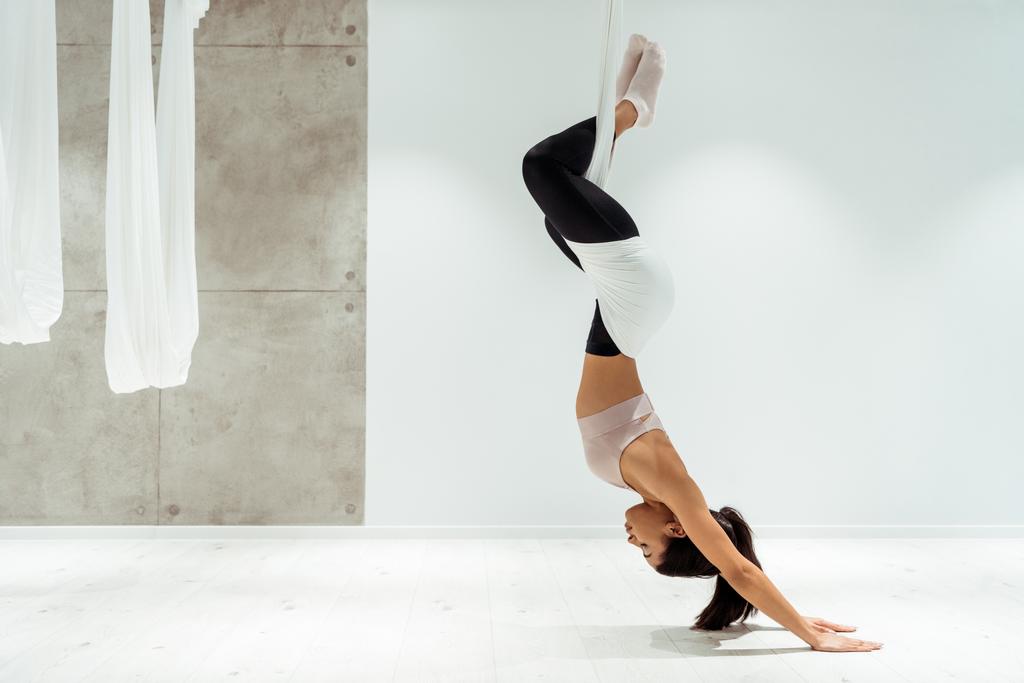 Спортивная девушка расслабляется во время практики антигравитационной йоги и инверсии позиции в студии йоги
 - Фото, изображение