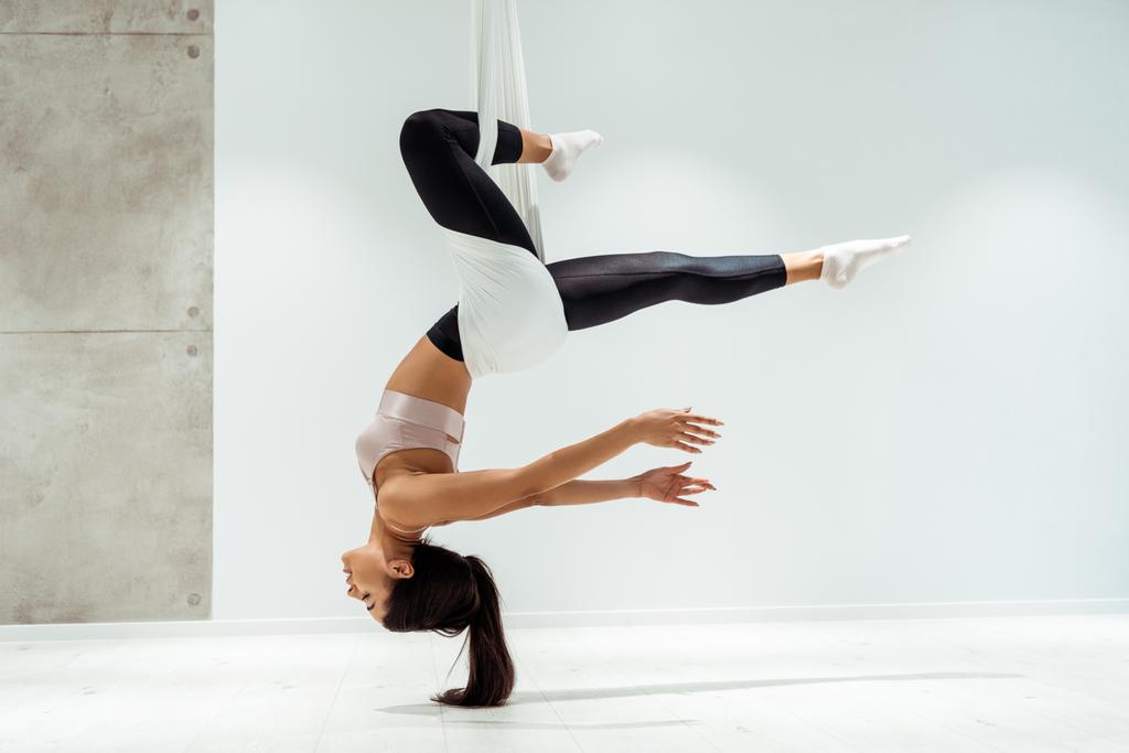 Красивая расслабленная девушка практикует антигравитационную йогу в инверсии позиции в студии
 - Фото, изображение