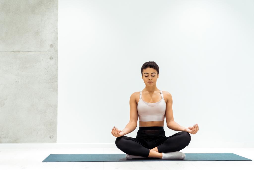 Расслабленная девушка с закрытыми глазами медитирует в позе лотоса в студии йоги
 - Фото, изображение