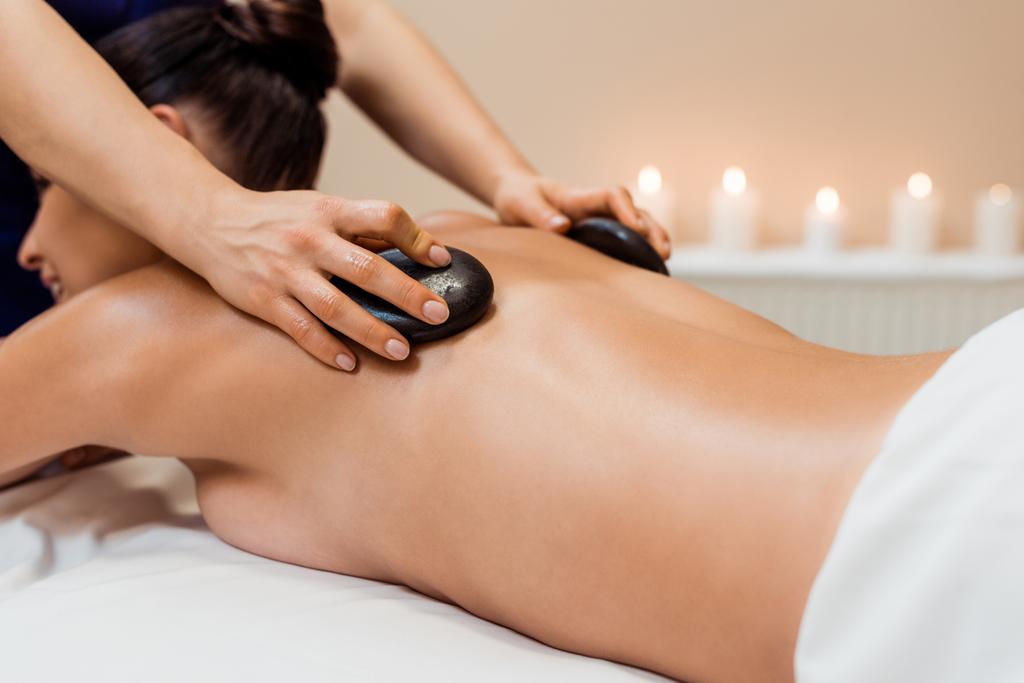 обрізаний знімок молодої жінки, що має масаж гарячим каменем у спа-центрі
 - Фото, зображення
