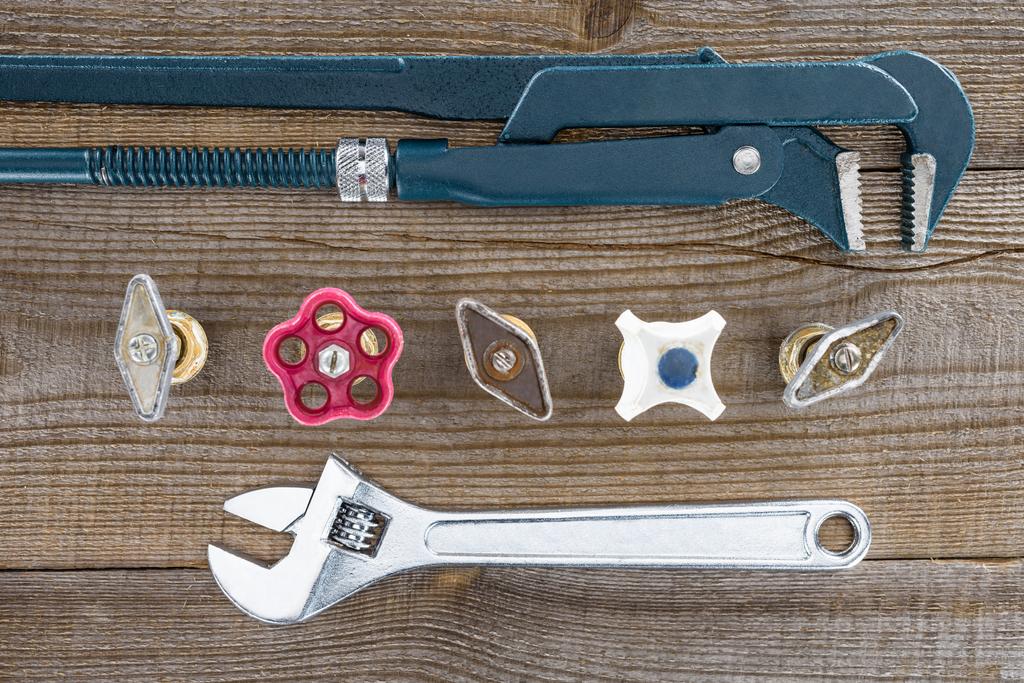 top view of plumber wrenches and various plumbing valves on rustic wooden tabletop - Photo, Image