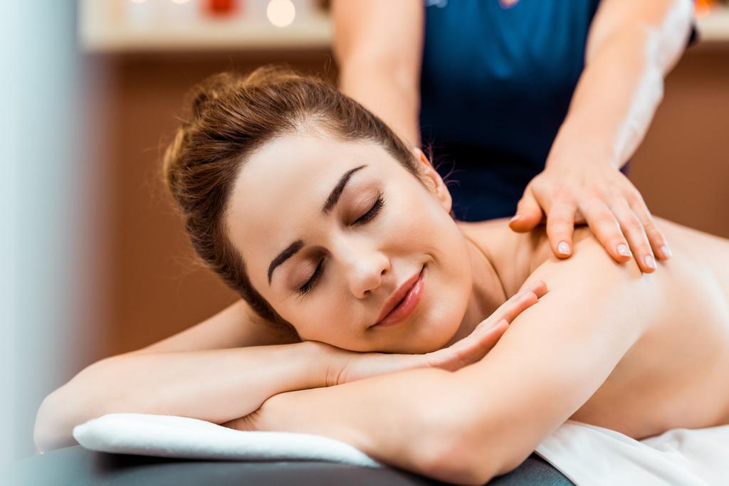 beautiful smiling young woman with closed eyes enjoying massage in spa  - Photo, Image