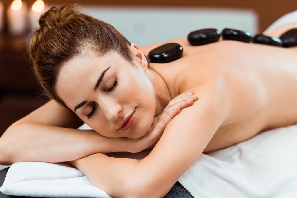 piękna młoda kobieta z zamkniętymi oczami, ciesząc się masaż gorącymi kamieniami w salonie spa  - Zdjęcie, obraz