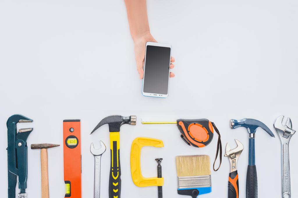 cropped shot of woman using smartphone with various tools lying on white - Photo, Image