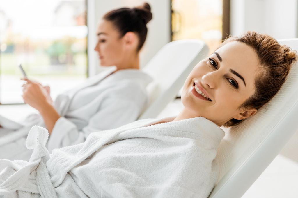 onnellinen nuori nainen kylpytakissa hymyilee kameralle, kun lepää kylpylässä
 - Valokuva, kuva