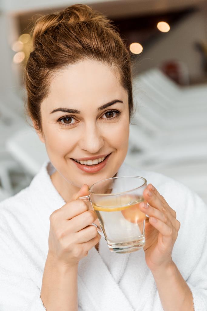onnellinen nuori nainen tilalla cup kasviperäisten juoman ja hymyillen kameran kylpylä
 - Valokuva, kuva