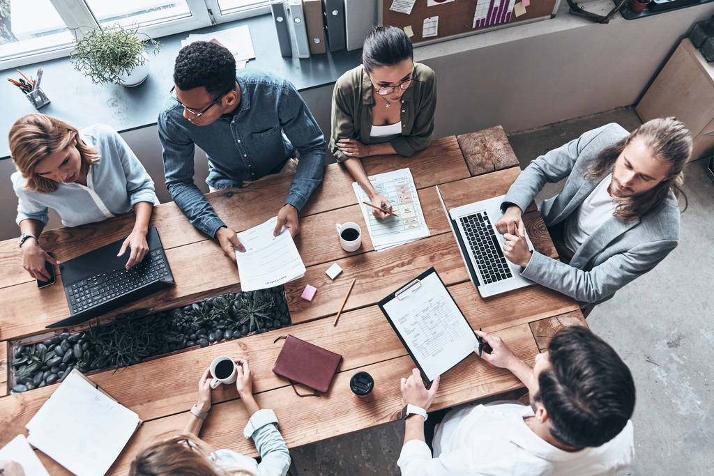 bovenaanzicht van mensen uit het bedrijfsleven brainstormen in moderne kantoor op houten tafel met laptops en documenten  - Foto, afbeelding