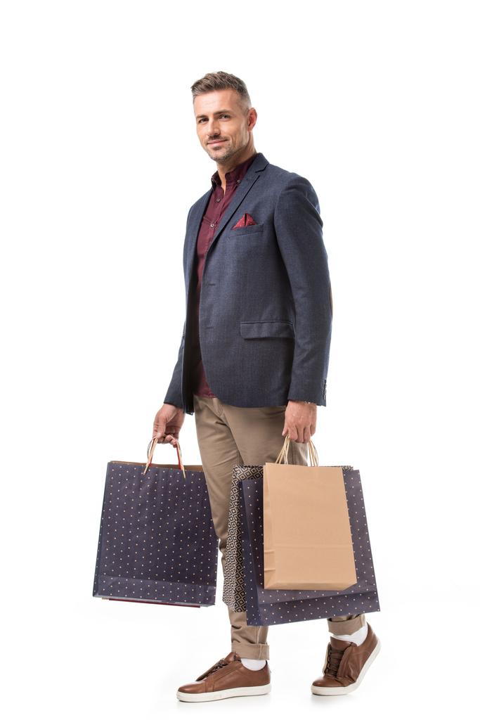 cheerful adult stylish man in jacket holding colorful shopping bags isolated on white - Photo, Image