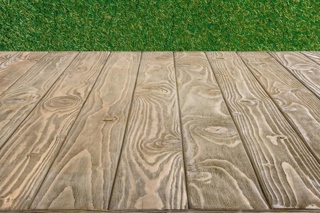  緑の草の背景に茶色の木製の板の表面 - 写真・画像