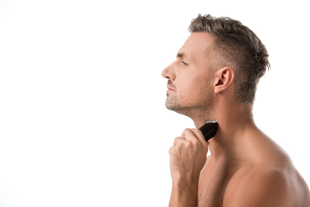 vista lateral del hombre adulto guapo afeitándose con trimmer eléctrico aislado en blanco
 - Foto, Imagen