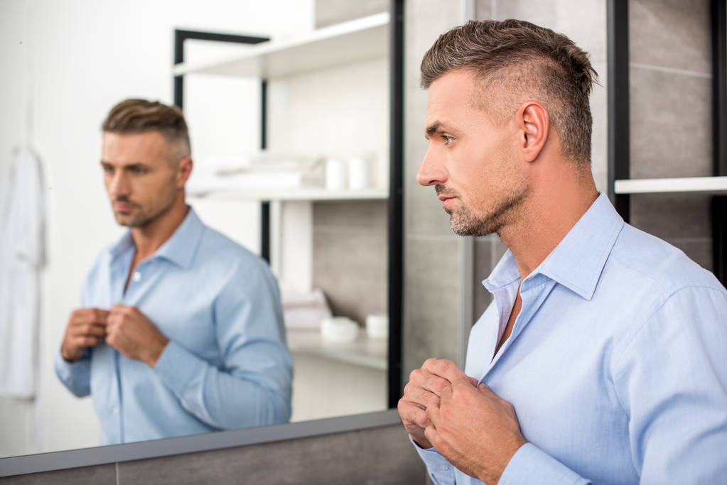 valikoiva painopiste aikuisten liikemies napittaa sininen paita kylpyhuoneessa kotona
 - Valokuva, kuva