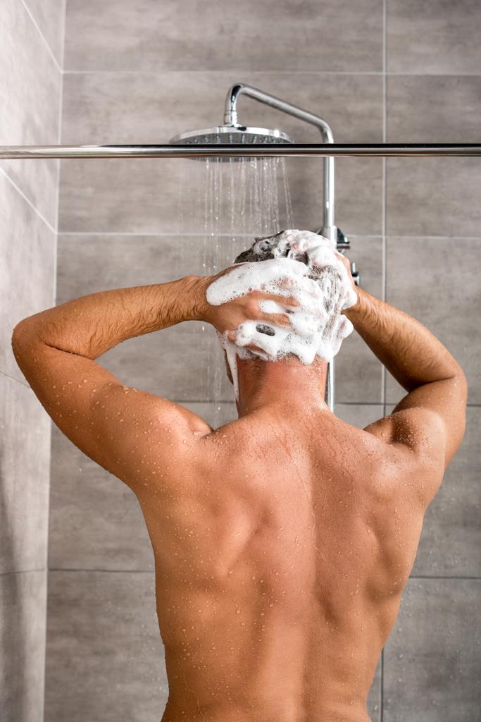 シャンプーとシャワーを浴びて髪を洗う人の背面図  - 写真・画像