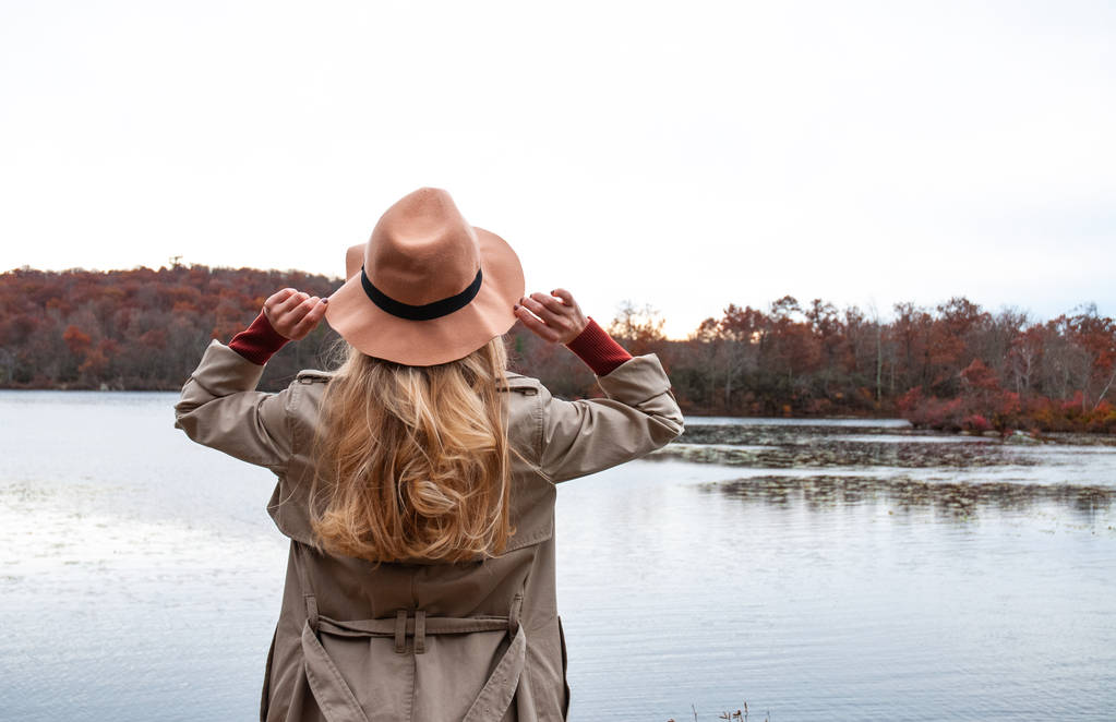 Γυναίκα με καπέλο και ζεστά ρούχα φθινόπωρο βλέπουν καταπληκτική λίμνη και δάσος, έννοια ταξίδι περιπλάνησης - Φωτογραφία, εικόνα