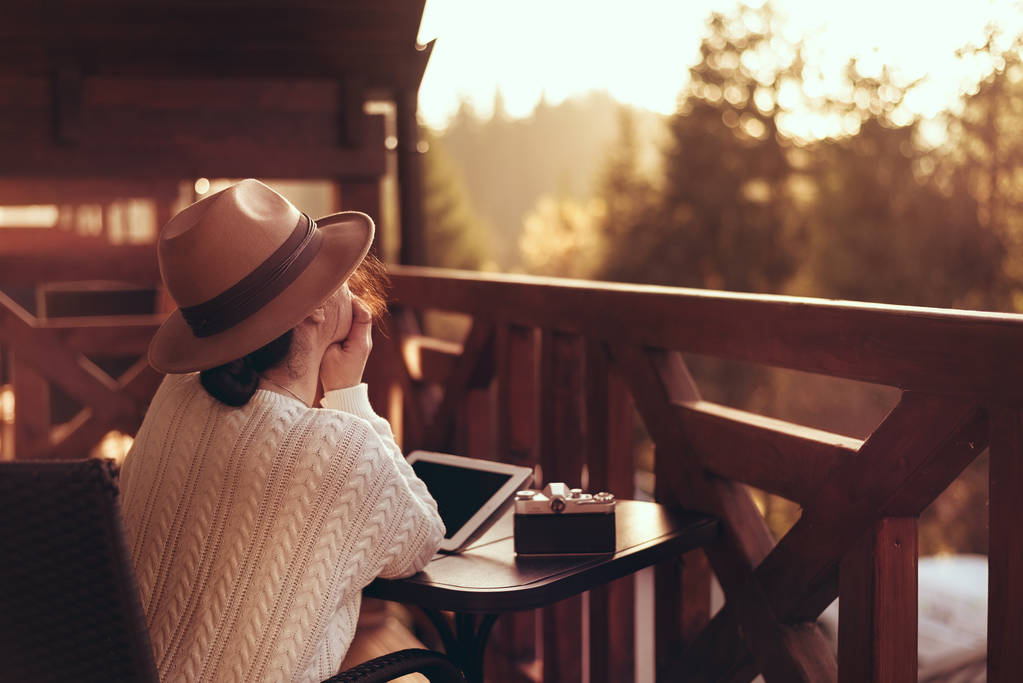 Jovem viajante senta-se no terraço com um tablet contra belas paisagens montanhosas durante a viagem
. - Foto, Imagem