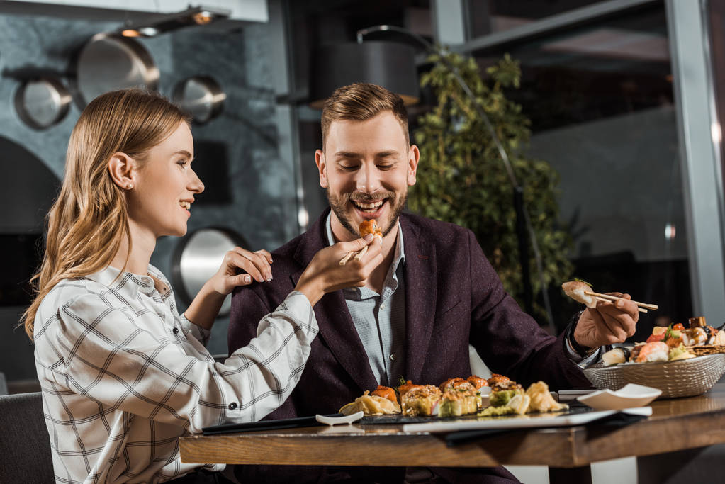 Attractive young adult woman feeding her handsome boyfriend in restaurant - Photo, Image