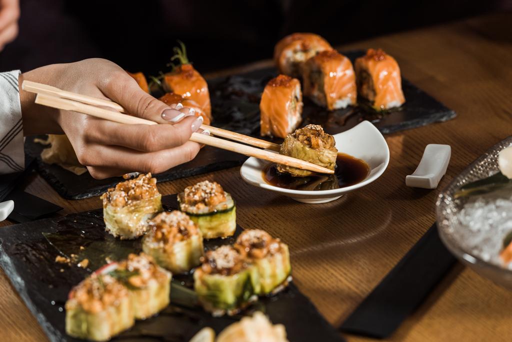 Partial view of woman dipping sushi in soy sauce with chopsticks - Photo, Image