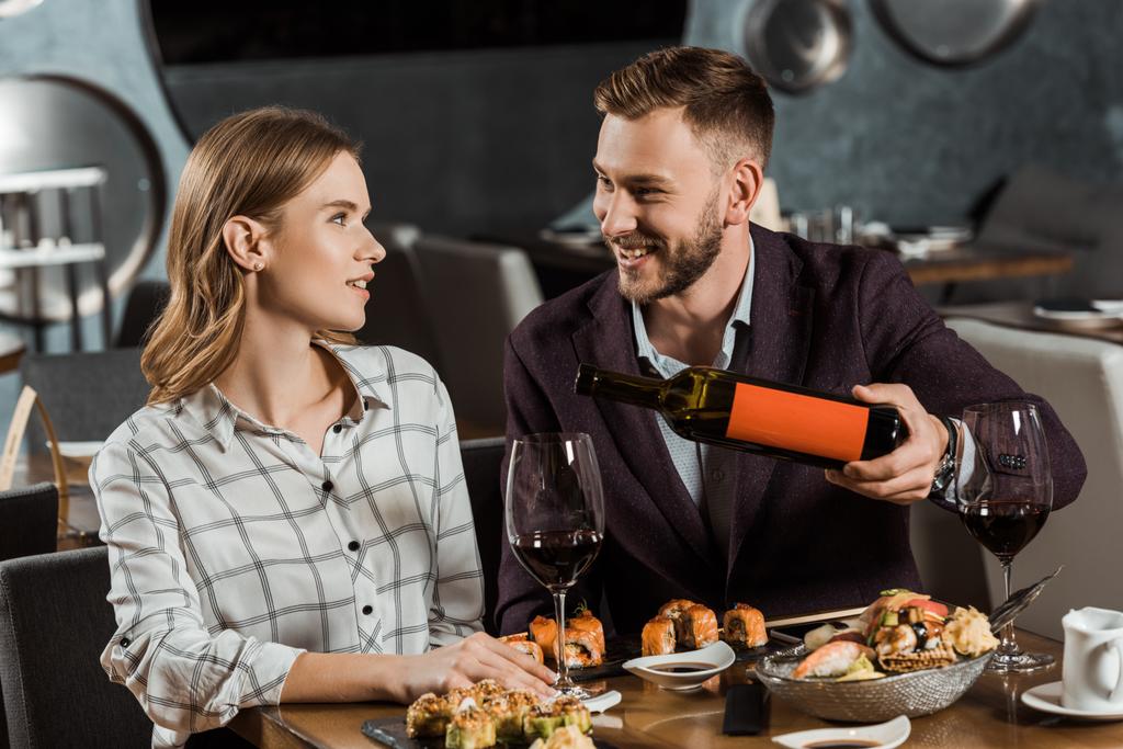 Happy νεαρό ζευγάρι ενηλίκων έχοντας δείπνο, ενώ ο άνθρωπος έκχυση κρασιού σε ποτήρια στο εστιατόριο - Φωτογραφία, εικόνα