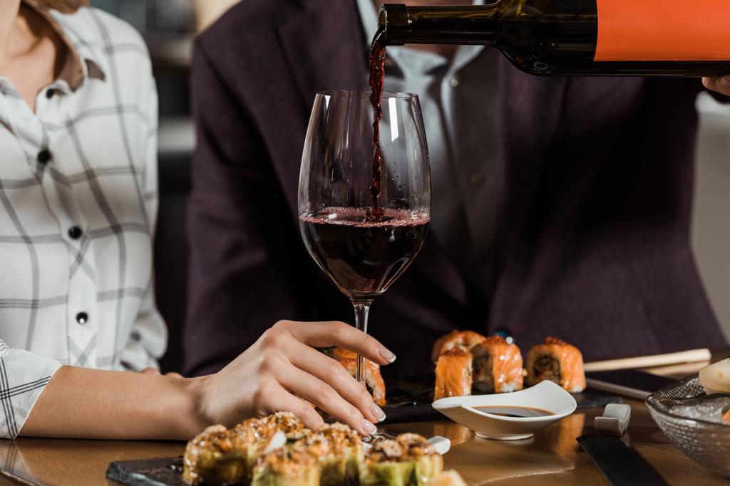 Обрізаний вид чоловіка, що поливає червоне вино в склянці в ресторані
 - Фото, зображення
