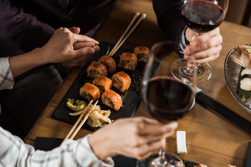 Vue partielle du couple se tenant la main tout en buvant du vin et en mangeant des sushis au restaurant
 - Photo, image