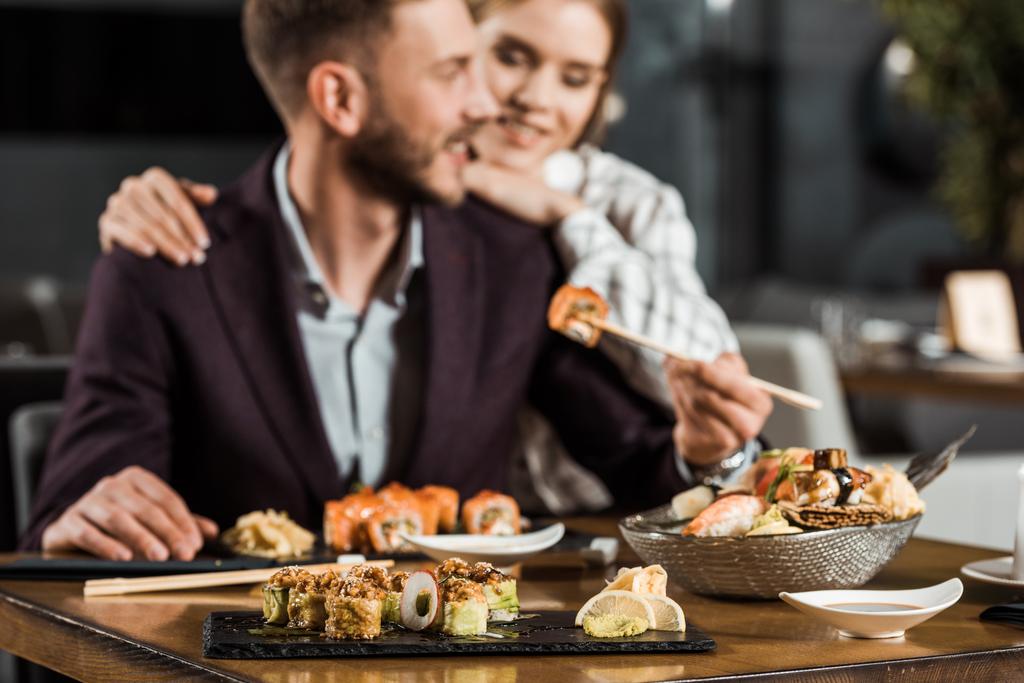 νεαρό ζευγάρι χαμογελώντας έχοντας το γεύμα και το φαγητό νόστιμο σούσι κυλίνδρους σε εστιατόριο - Φωτογραφία, εικόνα