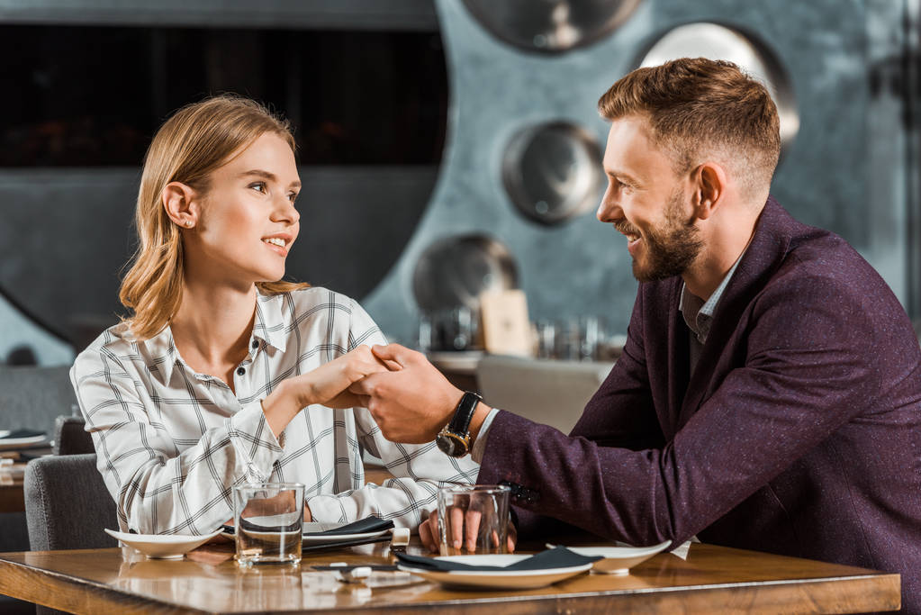 Pohledný mladý dospělý pár drží za ruce při posezení v restauraci - Fotografie, Obrázek