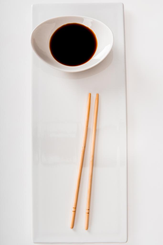 Top view of plate with soy sauce and chopsticks on white slate isolated on white - Photo, Image
